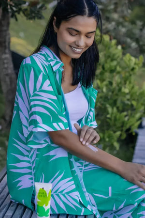 Woman applying natural mosquito repellent cream outdoors, product tube visible in foreground